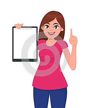 Happy smiling beautiful young woman holding / showing a blank clipboard and pointing up index finger.