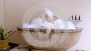 Happy smiling beautiful young woman in a luxurious spa hotel relaxes in a foam bathtub