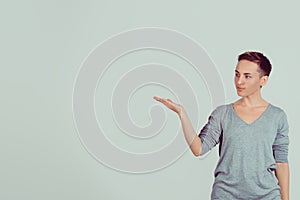 Happy smiling beautiful young woman shows a hand pointing to the side â€“ isolated light green wall background