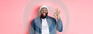 Happy smiling Black guy showing okay sign, approve and praise good offer, standing over pink background