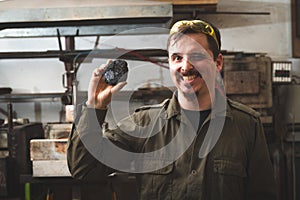 A happy smiling blacksmith holds an ore blank in his hand.