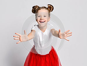 Happy smiling blonde kid girl in red skirt and white t-shirt is bending over with her arms outstretched towards us