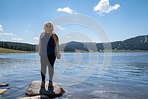 Happy smiling blonde woman stands on a rock in Meadowlark Lake in Wyoming, holding a phone