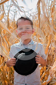 Happy smiling boy. Cute young 10 year old boy with black hat in his hands. Child in hte corn field - harvest season