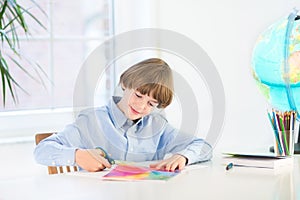 Happy smiling boy cutting colorful paper with scissors