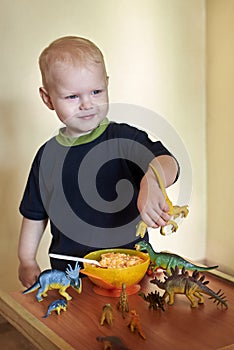 A happy smiling boy feeds a toy dinosaur porridge from a spoon