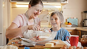 Happy smiling boy kissing his mother while making biscuit dough at home. Children cooking with parents, little chef