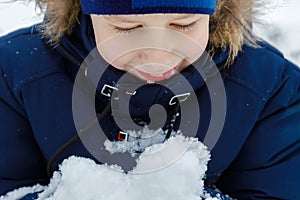 A happy, smiling boy is looking at the snow heap in his hand enjoying the outdoor winter pastime