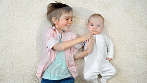 Happy smiling boy lying with his baby brother on carpet and having fun. Children happiness and family relationships.