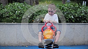 Happy smiling boy outdoors, child playing on a swing in the park. Child emotion concept. Summer sunny day Small children