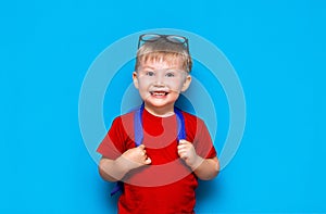 Happy smiling boy in red t-shirt with glasses on his head is going to school for the first time. Child with school bag. Kid on