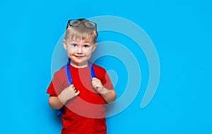 Happy smiling boy in red t-shirt with glasses on his head is going to school for the first time. Child with school bag. Kid on