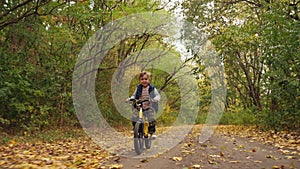 Happy smiling boy riding a bike in autumn park