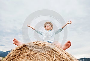 Happy smiling boy sits astride on the haystack