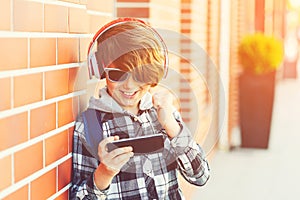 Happy smiling boy with smartphone playing game outside, over brick wall. New generation, leisure, children, technology. Schoolboy