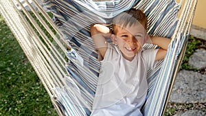 Happy smiling boy swinging and lying in hammock at garden. Summertime, happy childhood, vacation