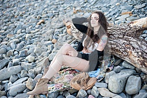 Happy smiling brunette brunette girl in boppy chic style sitting on gray stones