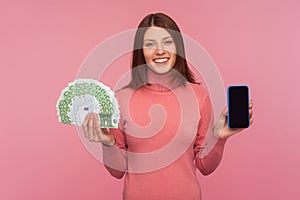 Happy smiling brunette woman holding fun of euro banknotes and cell phone with empty display in hands, mobile banking application