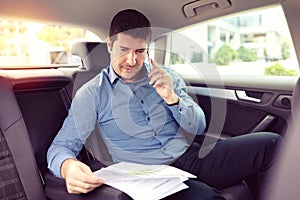 Happy smiling business man talking on phone doing business while siting in a taxi photo