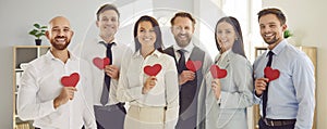 Happy smiling business people holding red hearts in hands standing together in a row in office