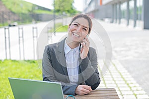 Happy smiling business woman talking on her mobile and browsing on a laptop while sitting at a table in a cafe on a