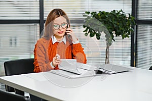 Happy smiling business woman at work talking on phone, sitting at her working place in office, copy space