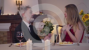 Happy smiling businessman in suit presenting bouquet of flowers to young woman. Excited beautiful girl smiling and