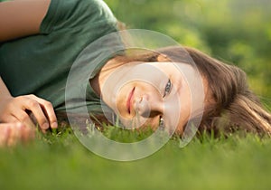 Happy smiling calm casual kid girl lying on the grass on nature summer background. Closeup