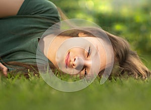 Happy smiling calm casual kid girl lying on the grass on nature summer background. Closeup