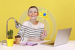 Happy smiling carefree woman holding paper windmill, pinwheel toy on stick, having fun on work place