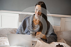 Happy smiling casual beautiful woman or girl working on a laptop sitting on the bed