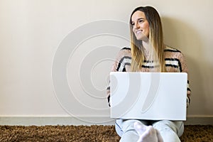 Happy smiling caucasian attractive woman looking at the horizon teleworking on laptop computer while sitting on the floor. Bright
