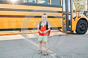 Happy smiling Caucasian boy elementary student with backpack near yellow bus on first September day. Education and back to school