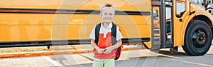 Happy smiling Caucasian boy student with backpack near yellow bus on first September day. Education and back to school in autumn