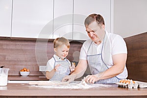 Happy smiling caucasian family in aprons cooking and kneading dough on a wooden