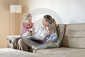 Happy smiling Caucasian mother with children reading book and having fun at home