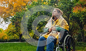 Happy smiling cheerful Caucasian girl on a wheelchair relaxing alone in autumn garden park