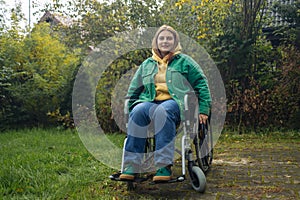 Happy smiling cheerful Caucasian girl on a wheelchair relaxing alone in autumn garden park