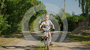 Happy smiling child boy is riding a bike on a country road in slow motion.