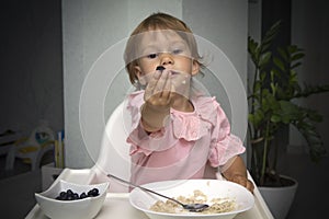 Happy, smiling child eating oatmeal with berries. The concept of a healthy breakfast for children, porridge with blueberries on