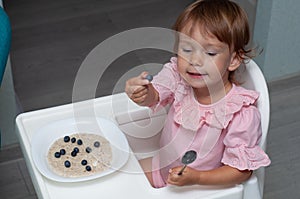 Happy, smiling child eating oatmeal with berries. The concept of a healthy breakfast for children, porridge with blueberries on