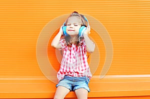 Happy smiling child enjoys listens to music in headphones over colorful orange