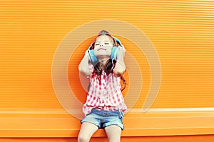 Happy smiling child enjoys listens to music in headphones over orange