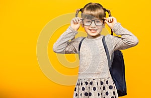 Happy smiling child girl in glasses is going to school for the first time. Child with school bag and with funny pigtails isolated