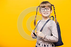 Happy smiling child girl in glasses is going to school for the first time. Child with school bag and with funny pigtails isolated