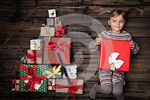 Happy smiling child girl in homewear keeping gift in vertical top view vintage wood with christmas tree pine made of