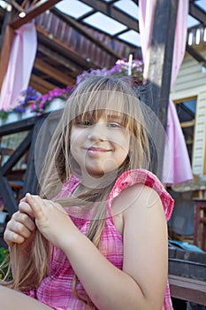 Happy smiling child girl in pink dress sitting outdoors at the dacha