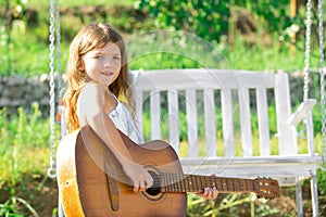 Happy smiling child girl play the guitar. Dreamy kids face. Smiling child playing outdoors in summer.