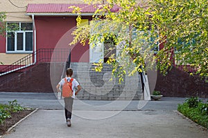 A happy smiling child goes to school. Back view of boy walking on stairs outdoors building background.