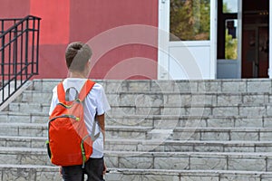 A happy smiling child goes to school. Back view of boy walking on stairs outdoors building background